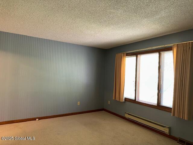 unfurnished room featuring light colored carpet, a textured ceiling, baseboards, a baseboard radiator, and visible vents