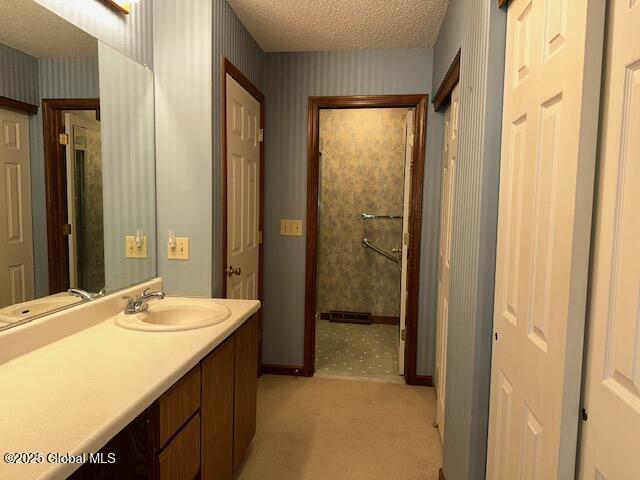 bathroom featuring a textured ceiling, wallpapered walls, baseboards, and vanity