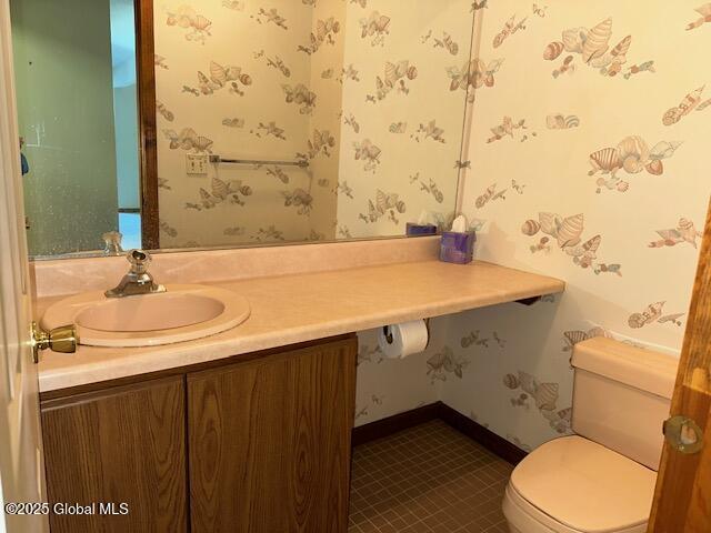half bath with vanity, tile patterned flooring, toilet, baseboards, and wallpapered walls