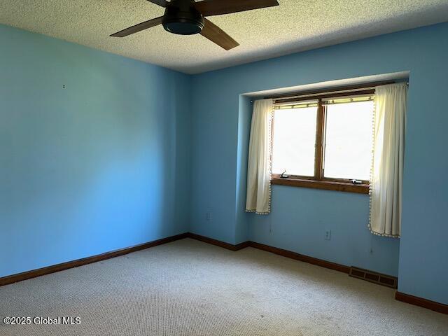 carpeted empty room with baseboards, ceiling fan, a textured ceiling, and visible vents