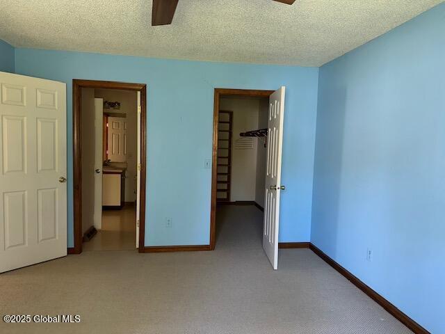 unfurnished bedroom with light carpet, a textured ceiling, baseboards, a spacious closet, and a closet