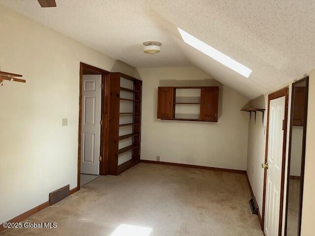 bonus room featuring baseboards, lofted ceiling with skylight, a textured ceiling, and light colored carpet
