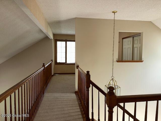corridor with a textured ceiling, lofted ceiling with beams, carpet, and an upstairs landing