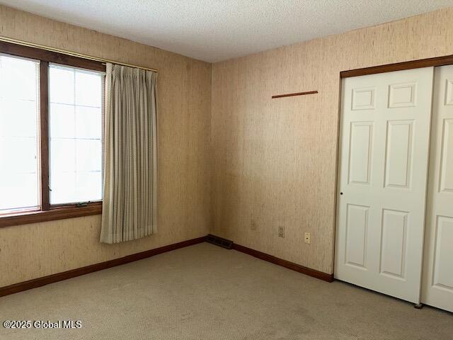 unfurnished room featuring a textured ceiling, baseboards, and light carpet