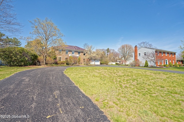 view of front facade featuring a chimney, a front yard, a garage, brick siding, and aphalt driveway