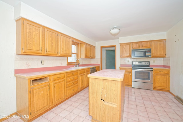 kitchen with decorative backsplash, a kitchen island, light countertops, a sink, and appliances with stainless steel finishes