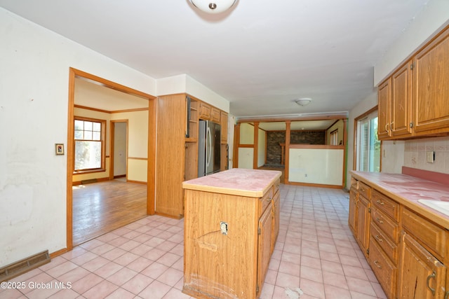 kitchen with visible vents, a center island, light countertops, freestanding refrigerator, and light tile patterned flooring