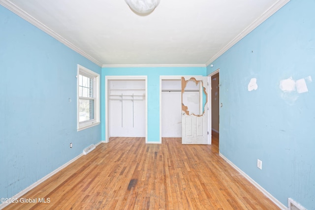 unfurnished bedroom with wood finished floors, crown molding, two closets, and visible vents