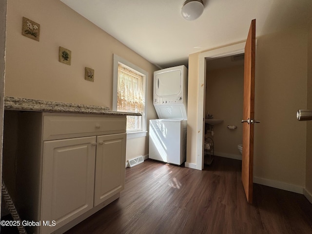 laundry room featuring dark wood-style flooring, baseboards, stacked washing maching and dryer, and visible vents