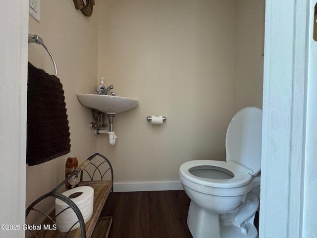 half bathroom with wood finished floors, toilet, and baseboards