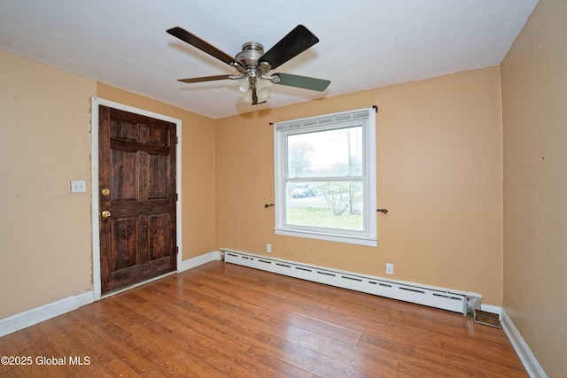 empty room with baseboards, wood finished floors, a ceiling fan, and a baseboard radiator