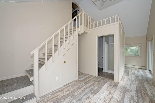 stairs featuring vaulted ceiling, wood finished floors, baseboard heating, and baseboards
