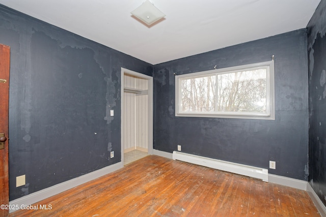 empty room featuring hardwood / wood-style flooring and a baseboard heating unit