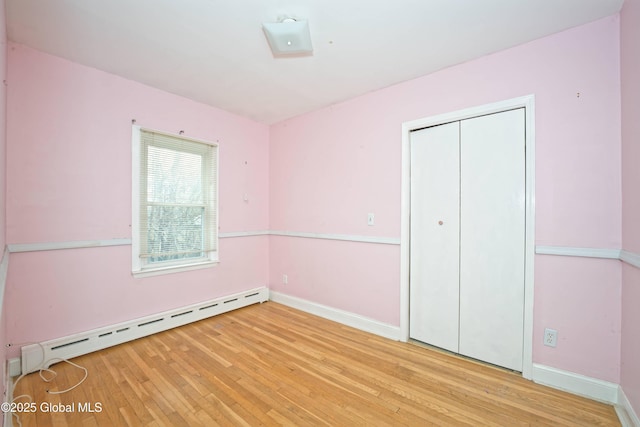 unfurnished bedroom featuring a baseboard heating unit, a closet, hardwood / wood-style floors, and baseboards