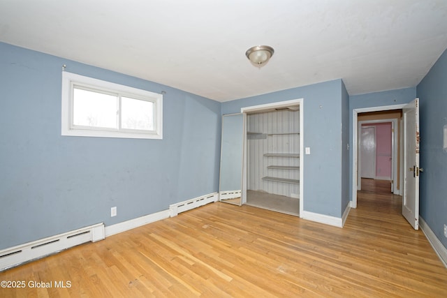 unfurnished bedroom with a baseboard heating unit, light wood finished floors, and baseboards