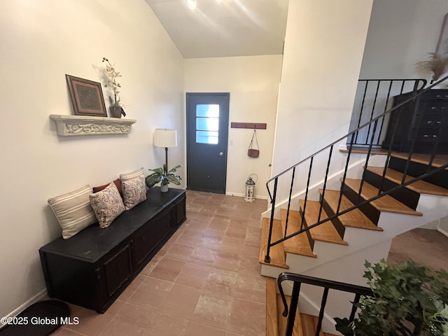 foyer entrance with stairway, baseboards, and lofted ceiling