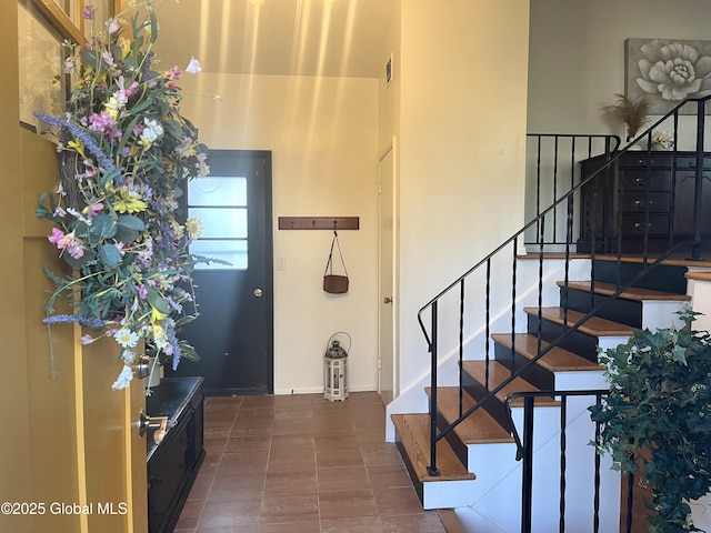 tiled foyer entrance with stairway, baseboards, and a towering ceiling
