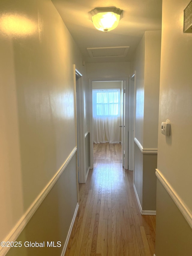 corridor featuring light wood-type flooring, attic access, and baseboards