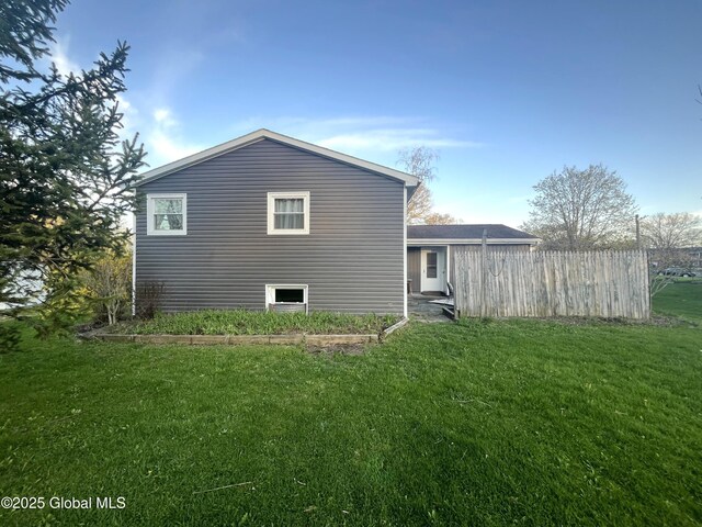 rear view of property featuring a lawn and fence