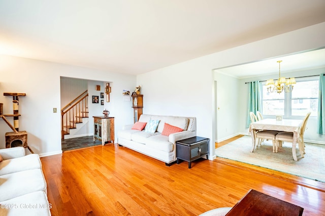 living room featuring an inviting chandelier, stairway, wood finished floors, and baseboards