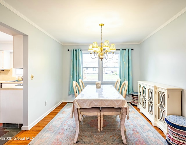 dining area with wood finished floors, a chandelier, crown molding, and baseboards