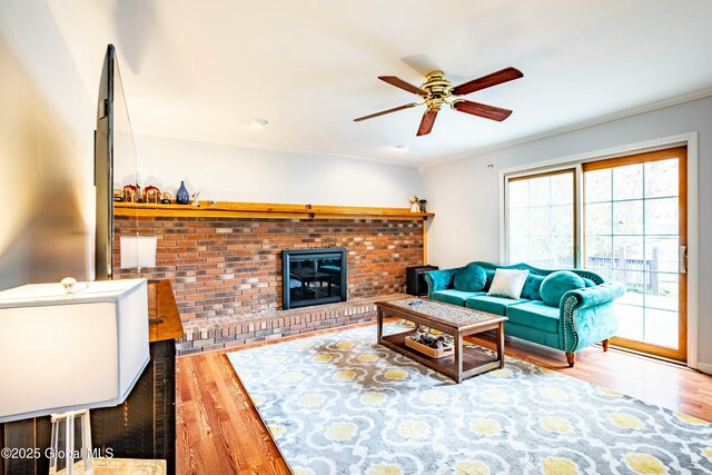 living area with wood finished floors, ceiling fan, ornamental molding, and a brick fireplace