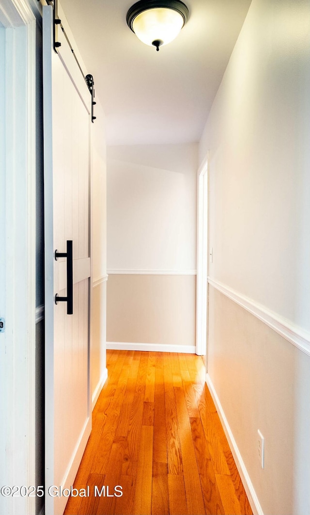 hall featuring a barn door, light wood finished floors, and baseboards