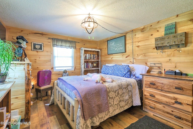 bedroom featuring a textured ceiling, wood walls, and wood finished floors