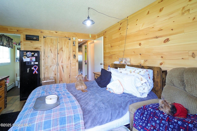 bedroom with a baseboard heating unit, wood walls, a textured ceiling, and wood finished floors
