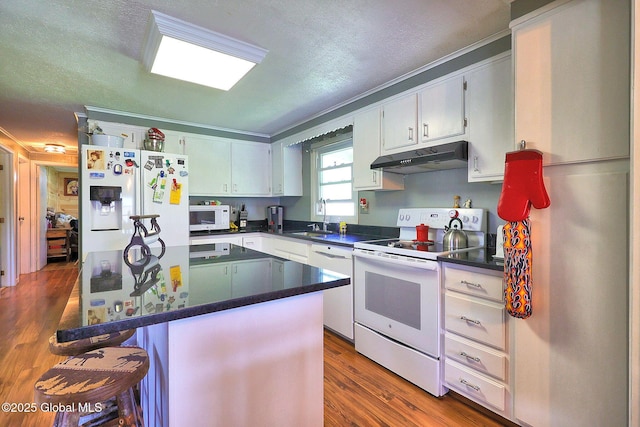 kitchen with a breakfast bar area, dark countertops, under cabinet range hood, white appliances, and dark wood-type flooring