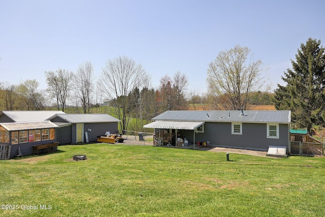 rear view of property with an outdoor structure, fence, metal roof, an outdoor fire pit, and a yard