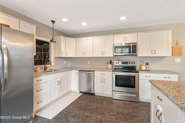 kitchen with light stone countertops, hanging light fixtures, a sink, stainless steel appliances, and white cabinetry