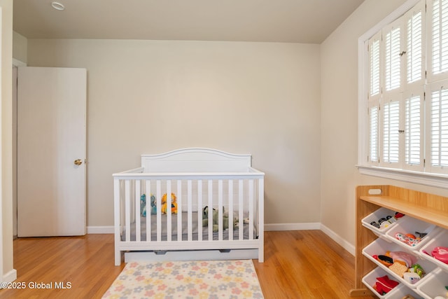 bedroom featuring a nursery area, baseboards, and wood finished floors