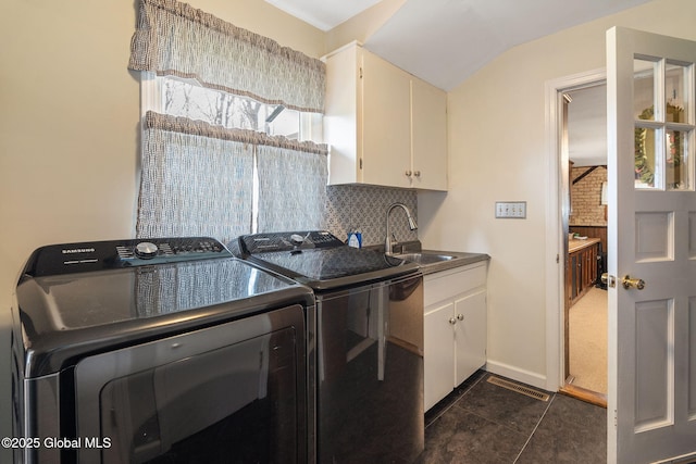 washroom featuring cabinet space, washing machine and clothes dryer, a sink, dark tile patterned flooring, and visible vents