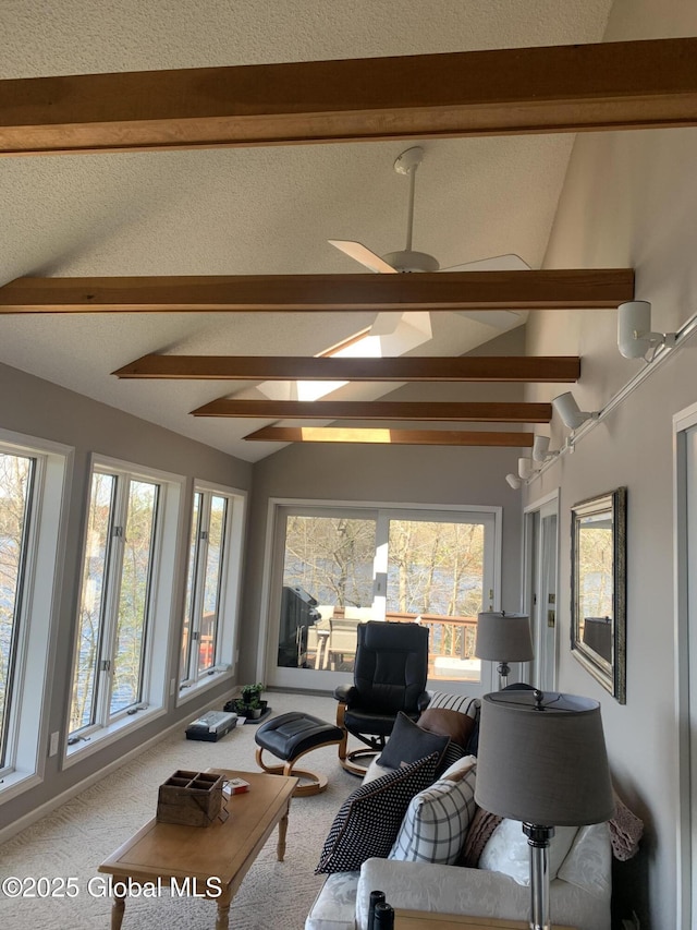 living area featuring a ceiling fan, plenty of natural light, carpet flooring, and vaulted ceiling with beams