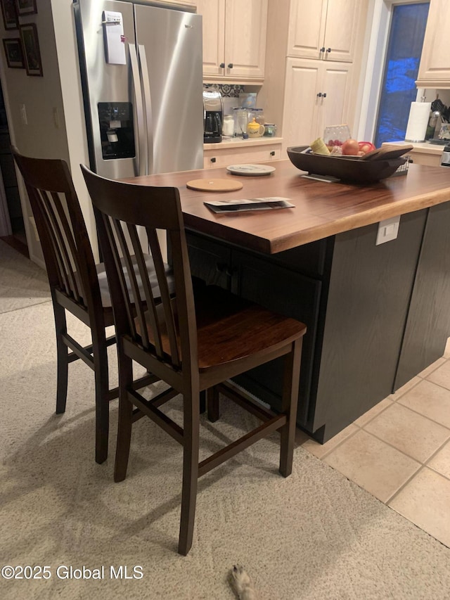 kitchen with butcher block countertops, a breakfast bar area, stainless steel fridge with ice dispenser, light carpet, and light tile patterned flooring