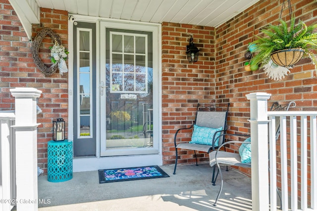 entrance to property featuring a porch and brick siding