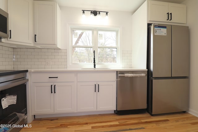 kitchen featuring decorative backsplash, white cabinets, a sink, light wood finished floors, and appliances with stainless steel finishes