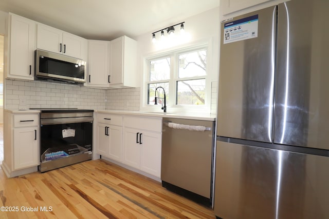 kitchen with light wood-type flooring, light countertops, tasteful backsplash, a sink, and appliances with stainless steel finishes