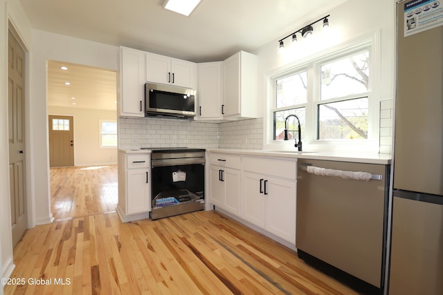 kitchen featuring white cabinets, a sink, light wood-style flooring, backsplash, and stainless steel appliances