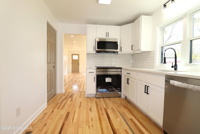 kitchen with appliances with stainless steel finishes, light countertops, white cabinetry, decorative backsplash, and light wood-type flooring