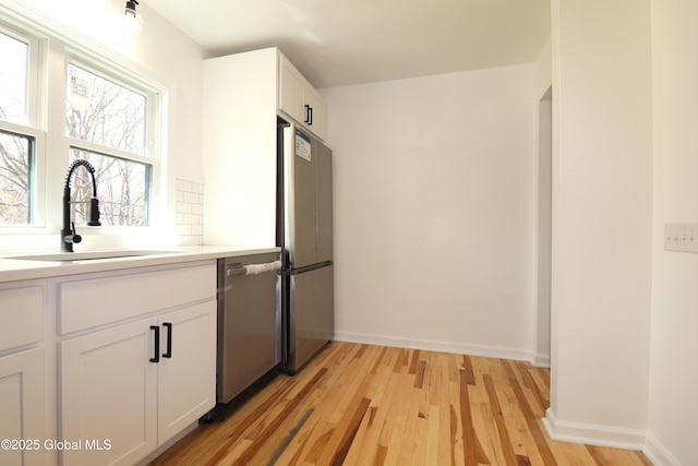 kitchen featuring white cabinets, appliances with stainless steel finishes, a sink, light wood finished floors, and light countertops