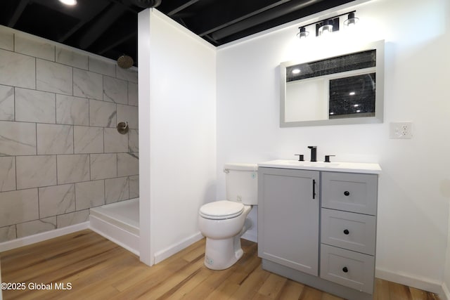 full bath with a tile shower, vanity, toilet, baseboards, and wood finished floors