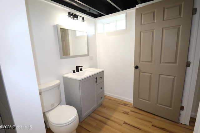 half bathroom with vanity, wood finished floors, and toilet
