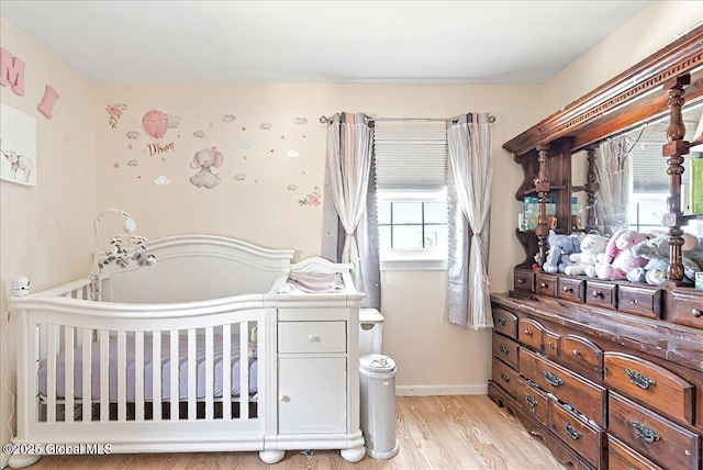 bedroom with a nursery area, baseboards, and light wood-type flooring