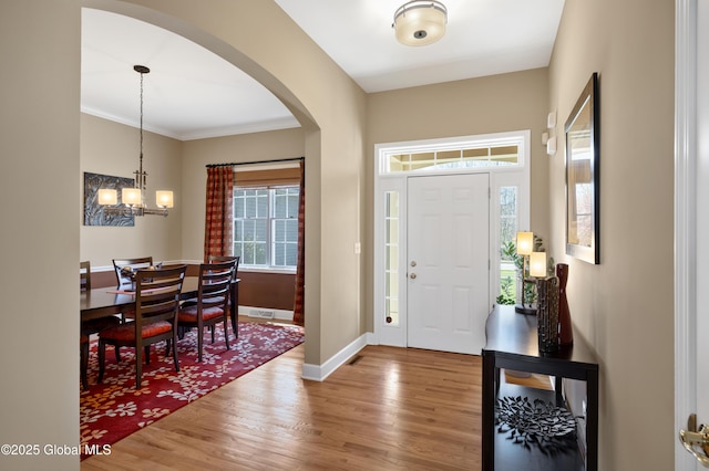 entrance foyer with crown molding, arched walkways, wood finished floors, baseboards, and a chandelier