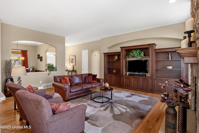 living area with arched walkways, light wood-style flooring, and visible vents