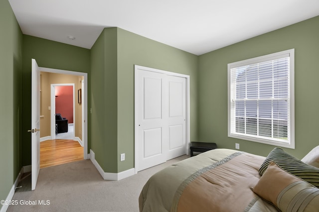 bedroom with baseboards, a closet, and light colored carpet