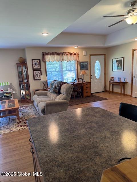 living room featuring ceiling fan, a tray ceiling, and wood finished floors