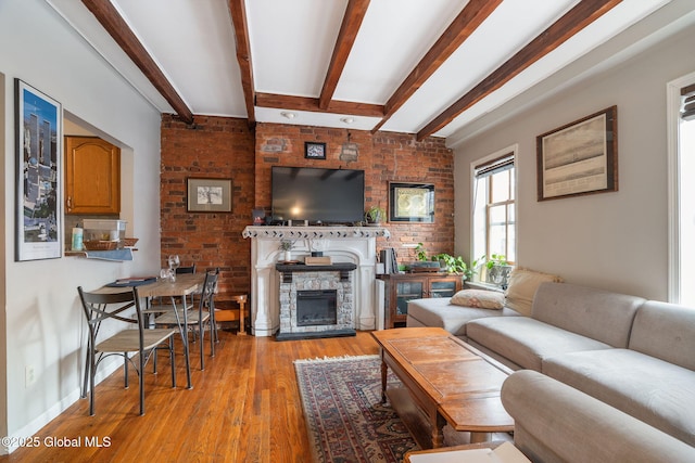 living room with a stone fireplace, brick wall, beam ceiling, baseboards, and light wood-style floors
